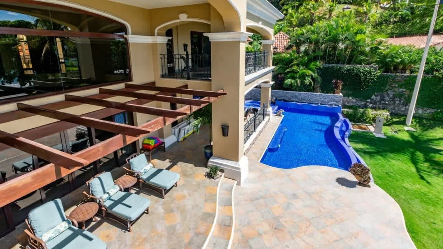 A sunny patio with outdoor seating overlooks a bright blue swimming pool.