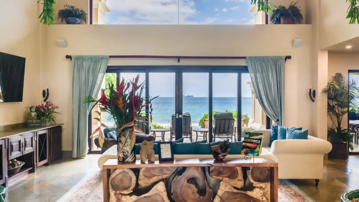 A bright living room opens onto a seaside view through wide glass doors.