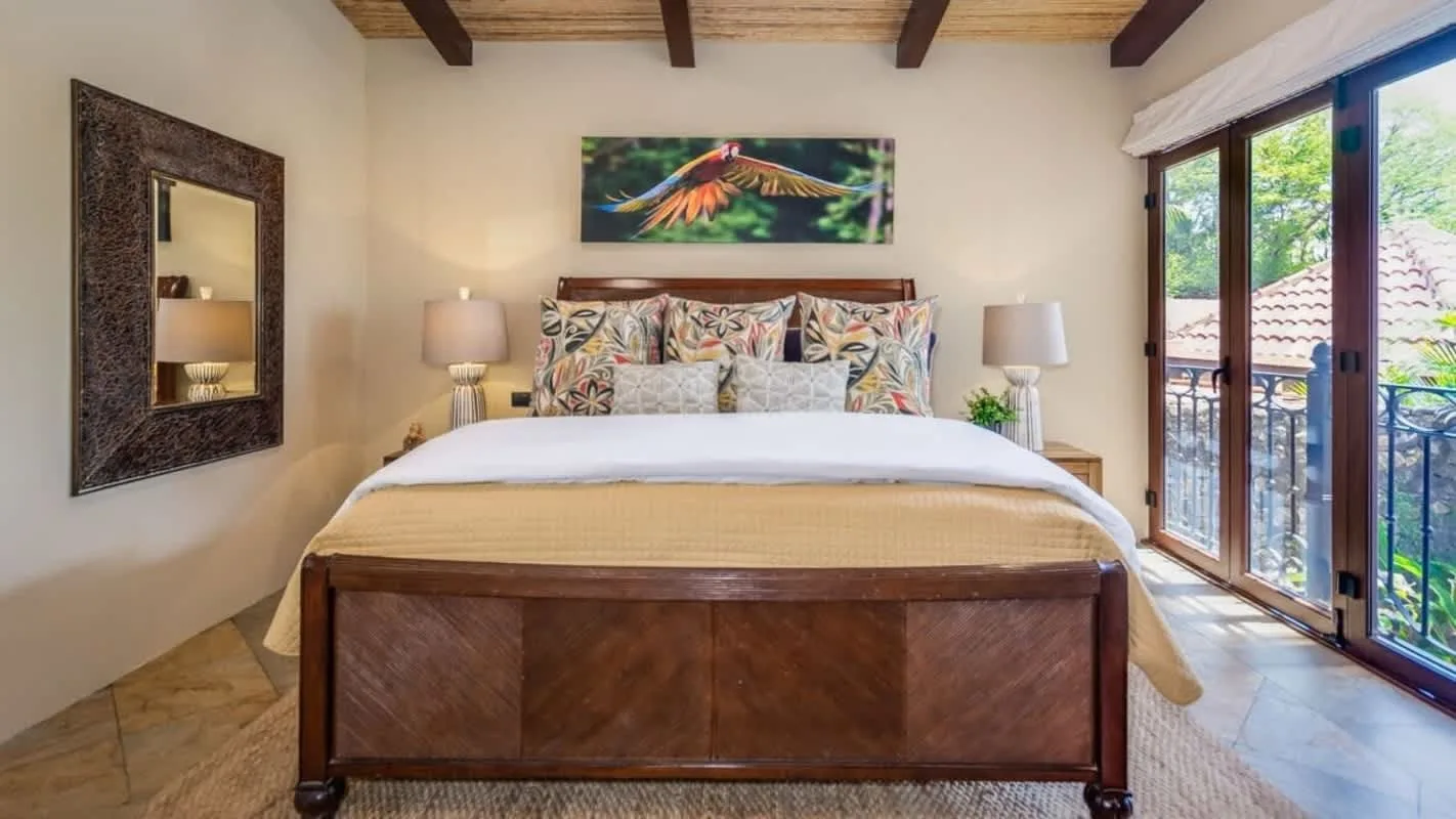 A bedroom with a large bed, patterned pillows, and glass doors opening onto a balcony.