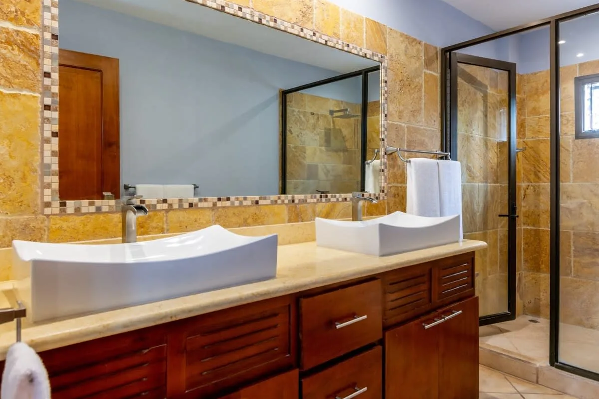 A bathroom vanity with two vessel sinks sits beside a glass shower.