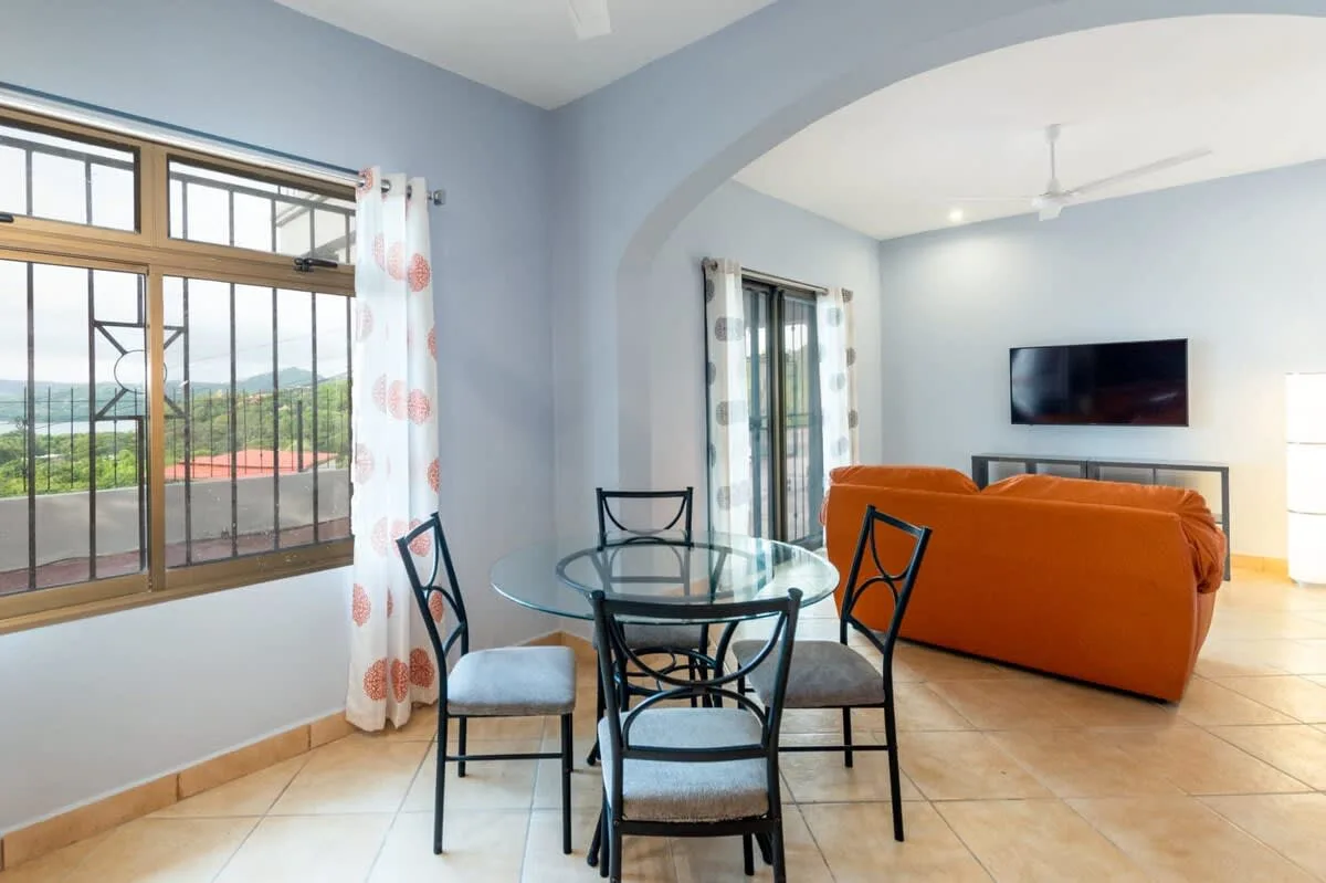 A living room with an orange sofa, television, and glass dining table.