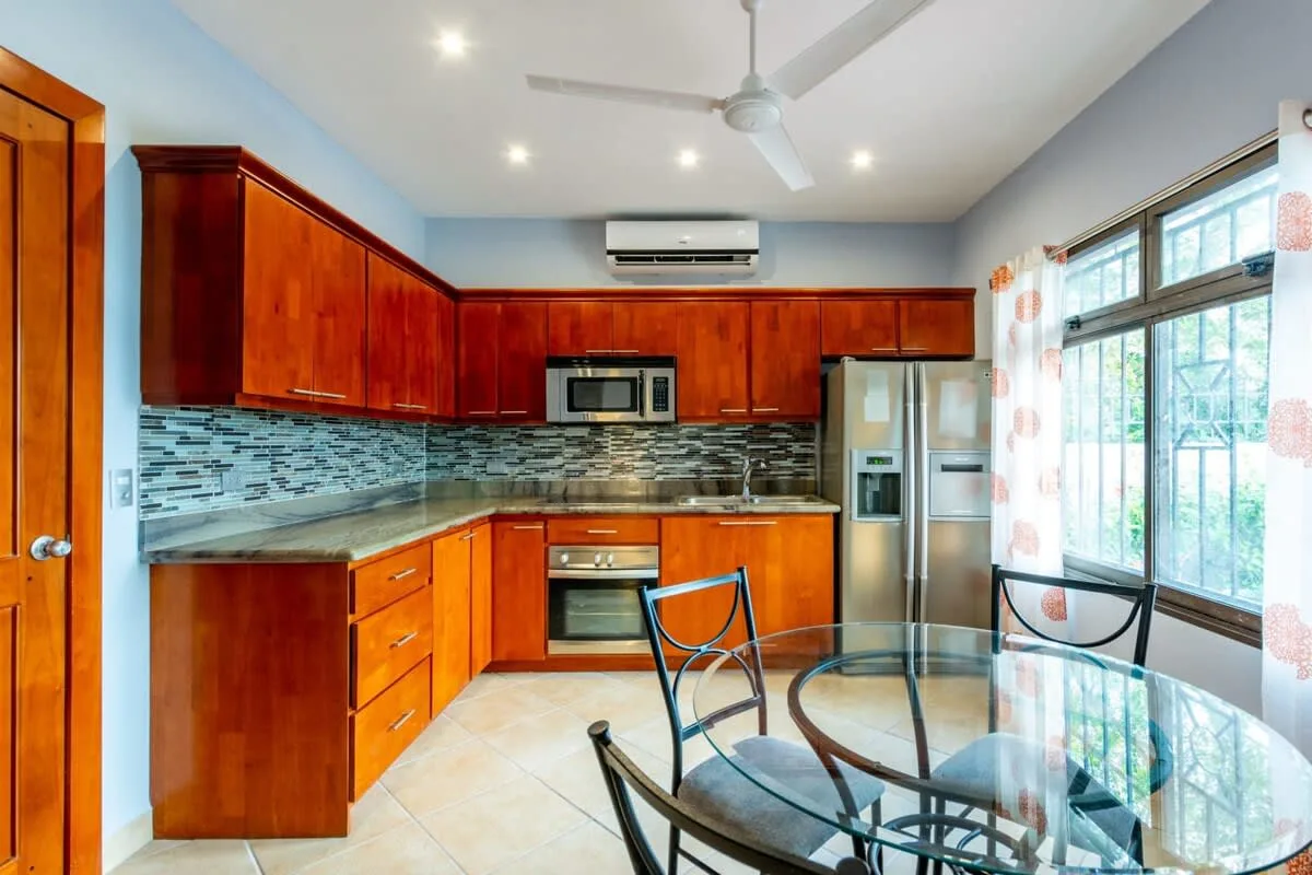 A bright kitchen with wooden cabinets, appliances, and a glass dining table.