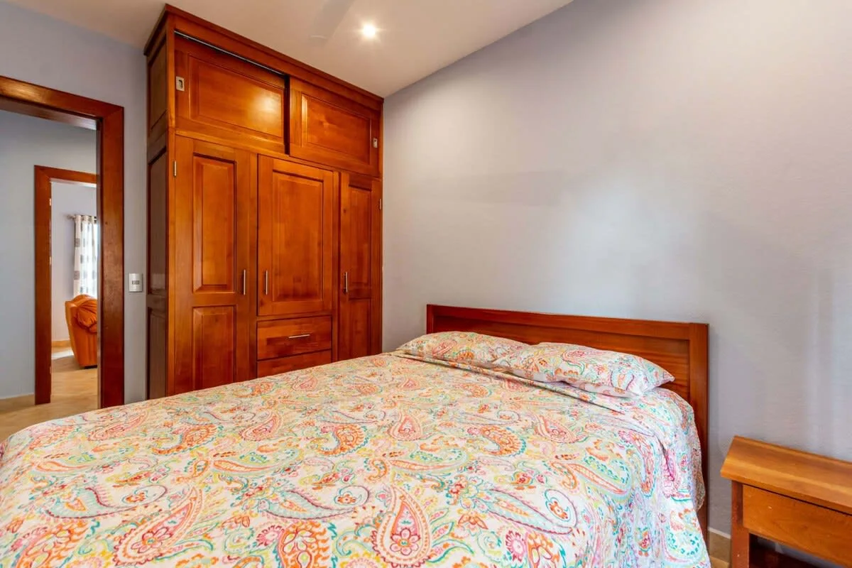 A bedroom with a bed covered in colorful patterned bedding beside a wooden wardrobe.