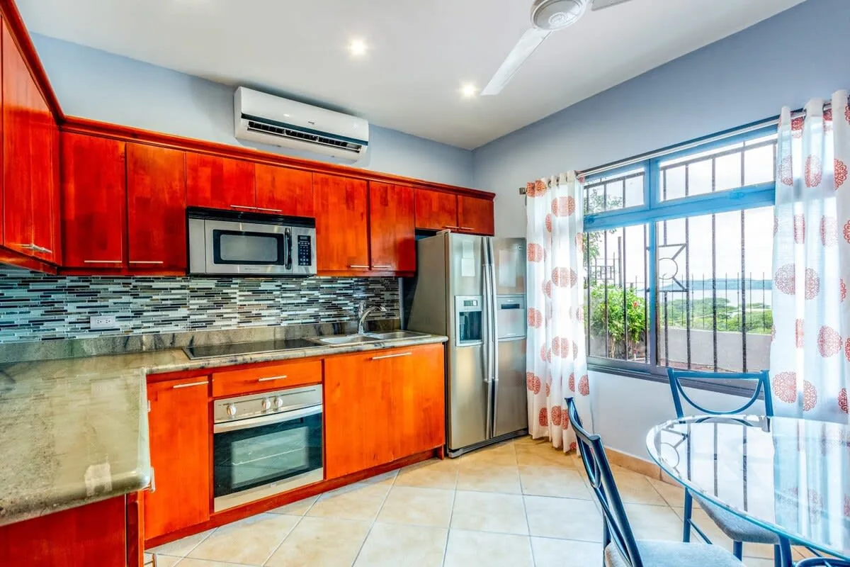 A bright kitchen with red cabinets, stainless steel appliances, and a dining table by the window.