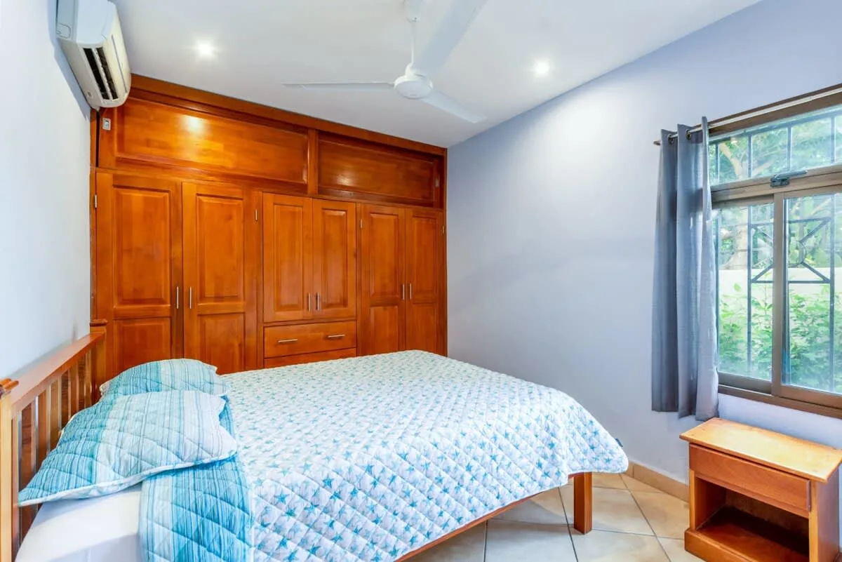 A bedroom with a bed, wooden built-in cabinets, and a curtained window.