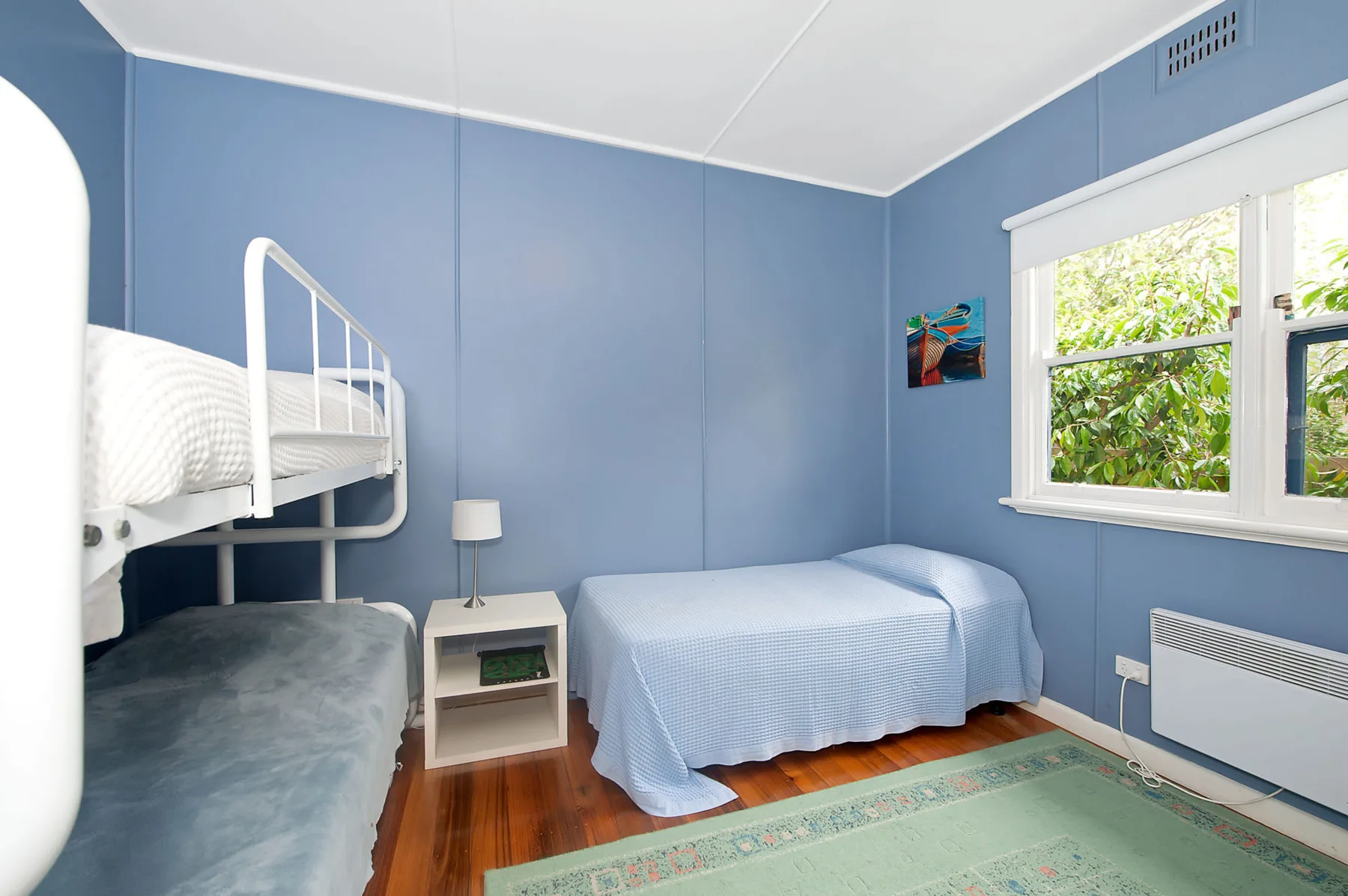 Un dormitorio azul con una litera, otra cama y una ventana.