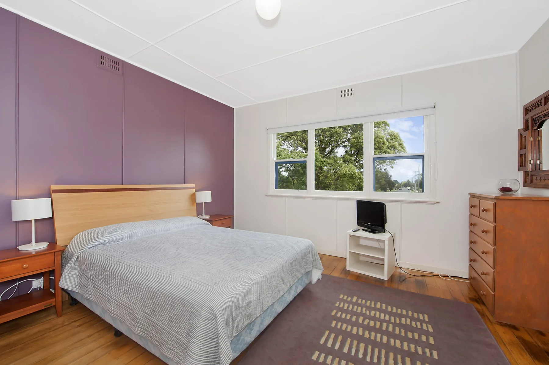 Un dormitorio con una cama junto a una ventana con vistas a árboles frondosos.