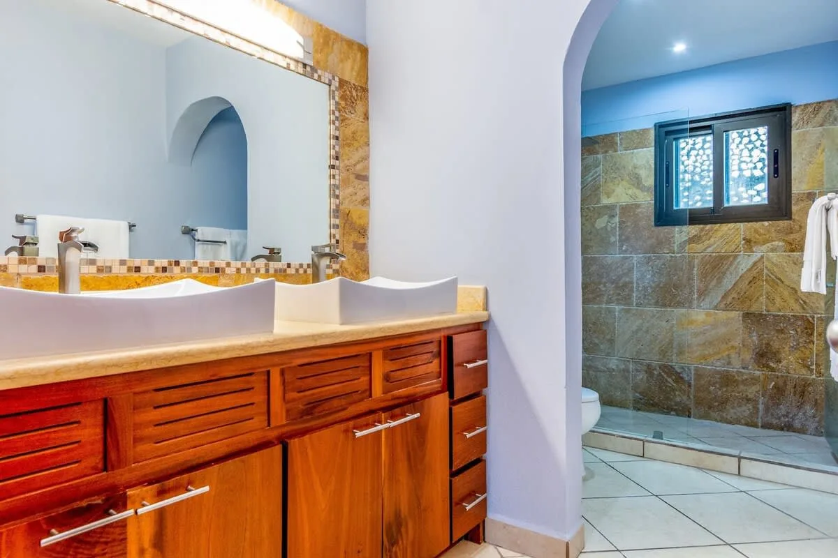 Un tocador de baño con un espejo grande está junto a una zona de ducha con azulejos.