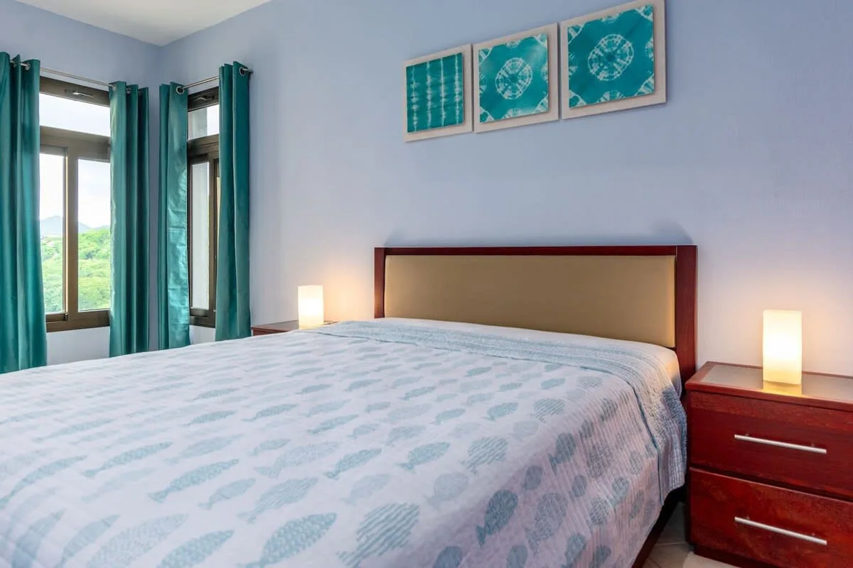 Un dormitorio con una cama grande, cortinas color turquesa y cuadros en la pared.