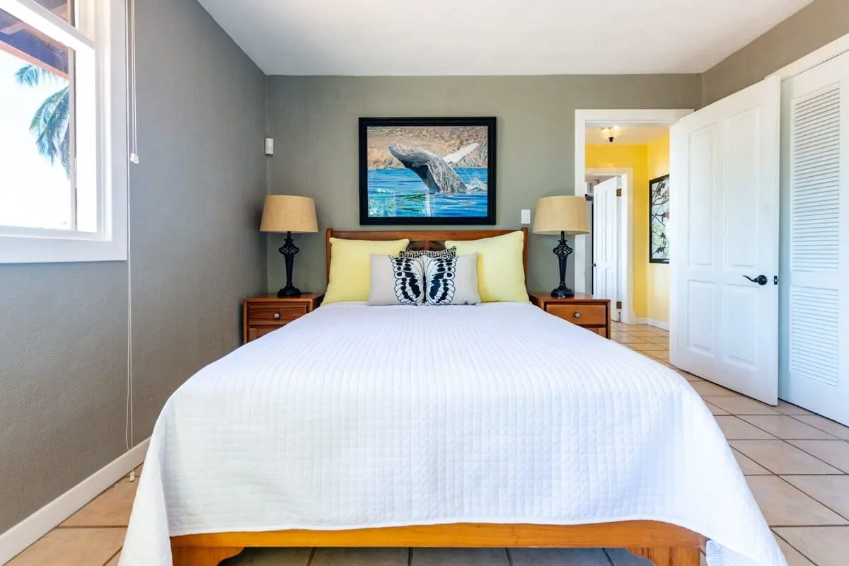 A bedroom with a bed, matching bedside lamps, and a framed ocean picture.