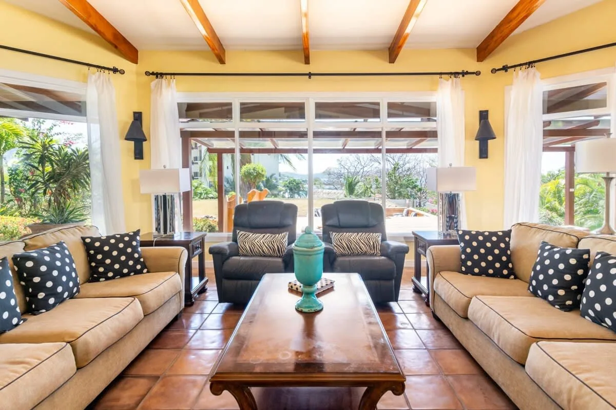 A bright living room has seating around a wooden coffee table and large windows.