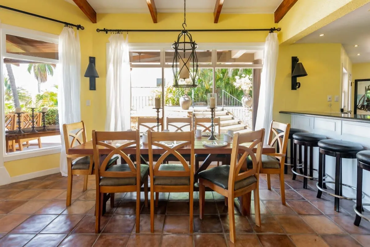 A dining area with a wooden table and chairs beside large windows.