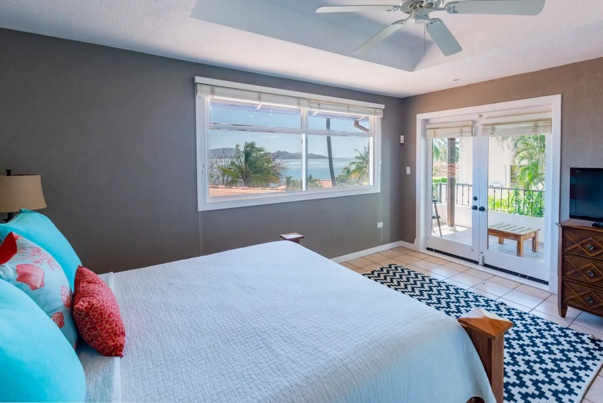 A bedroom with a large bed beside windows overlooking the water.