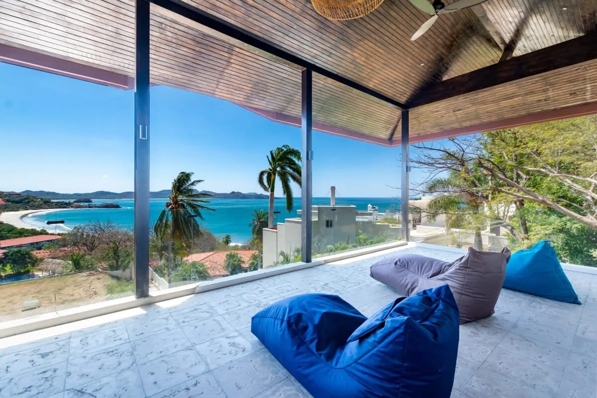 A covered terrace overlooks the ocean, with blue beanbag seating on the tiled floor.