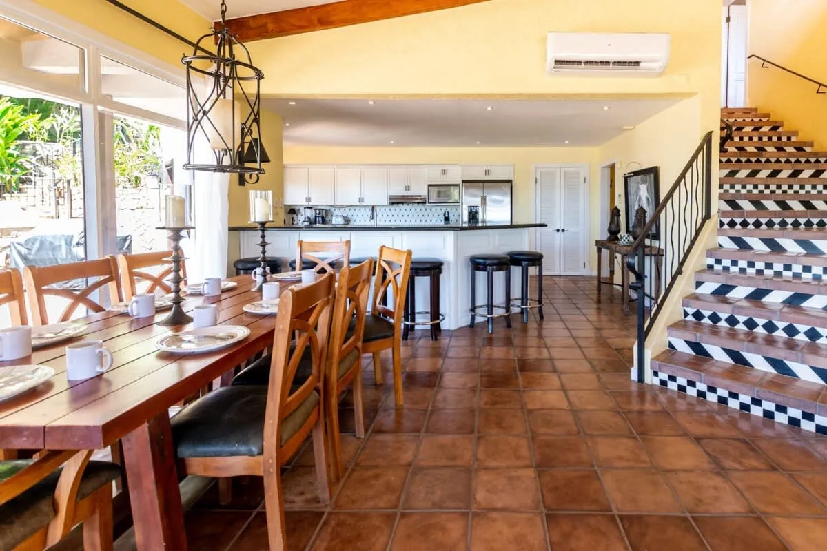 A dining area opens onto a kitchen, with a long wooden table and staircase.