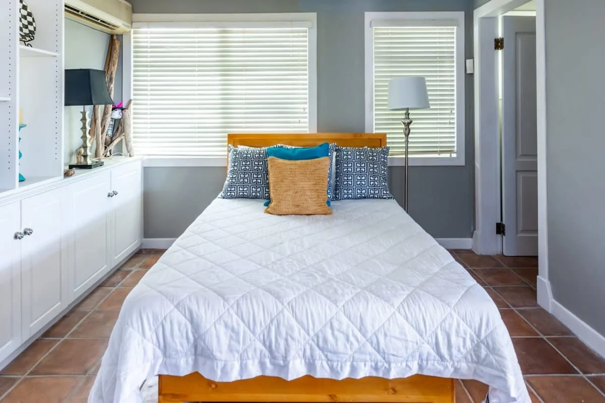 A bedroom with a neatly made bed between two windows.