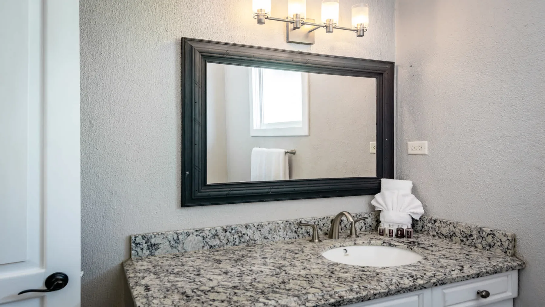 A bathroom vanity with a wide mirror and a granite-patterned countertop.