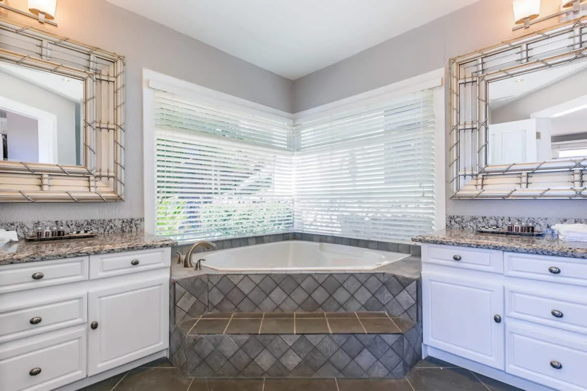 A bathroom with a corner bathtub beneath windows and vanities on both sides.