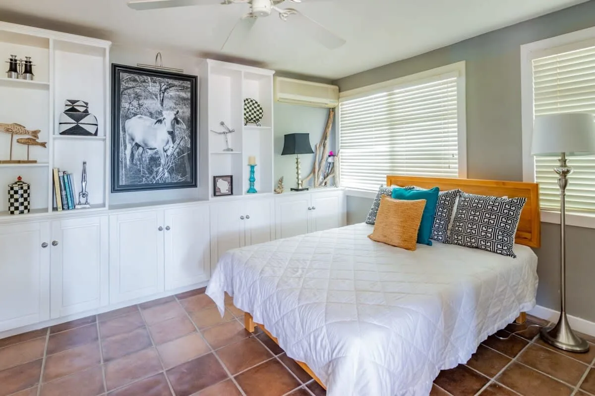 A bedroom with a bed, built-in shelving, and wide windows.