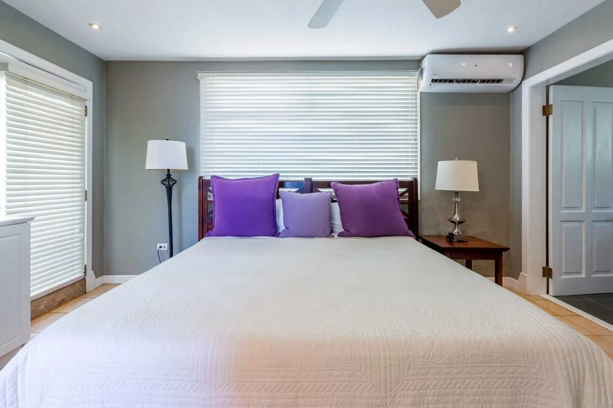 A bedroom with a bed beneath a wide window with closed blinds.