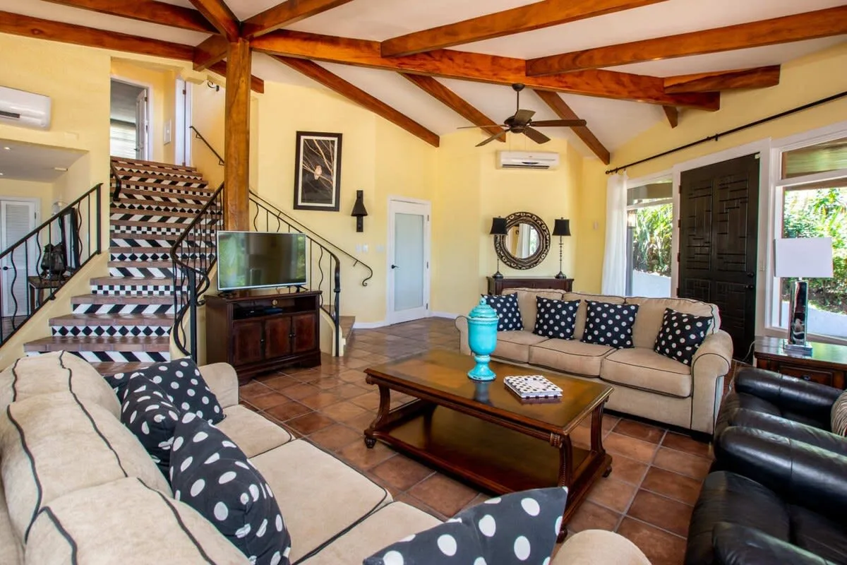 A living room with seating around a coffee table beneath exposed wooden ceiling beams.