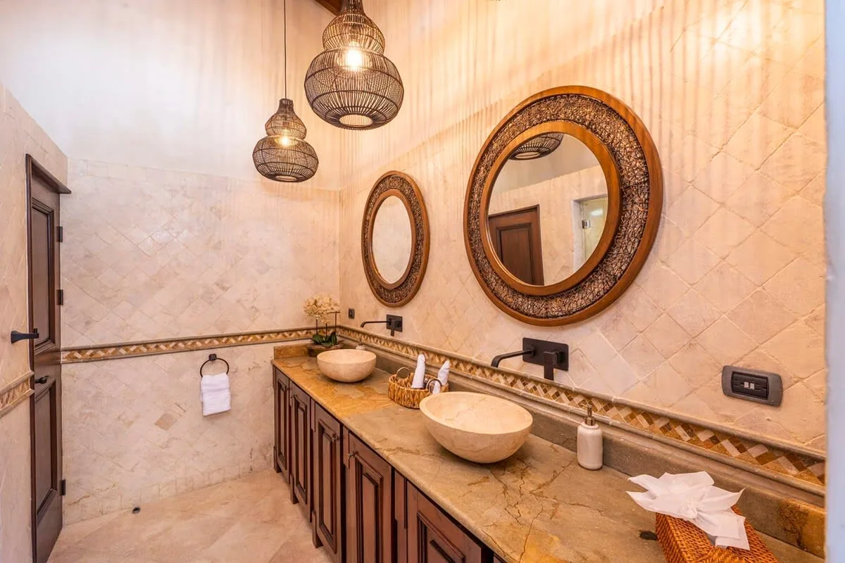 A bathroom vanity with two vessel sinks, decorative mirrors, and woven pendant lights.