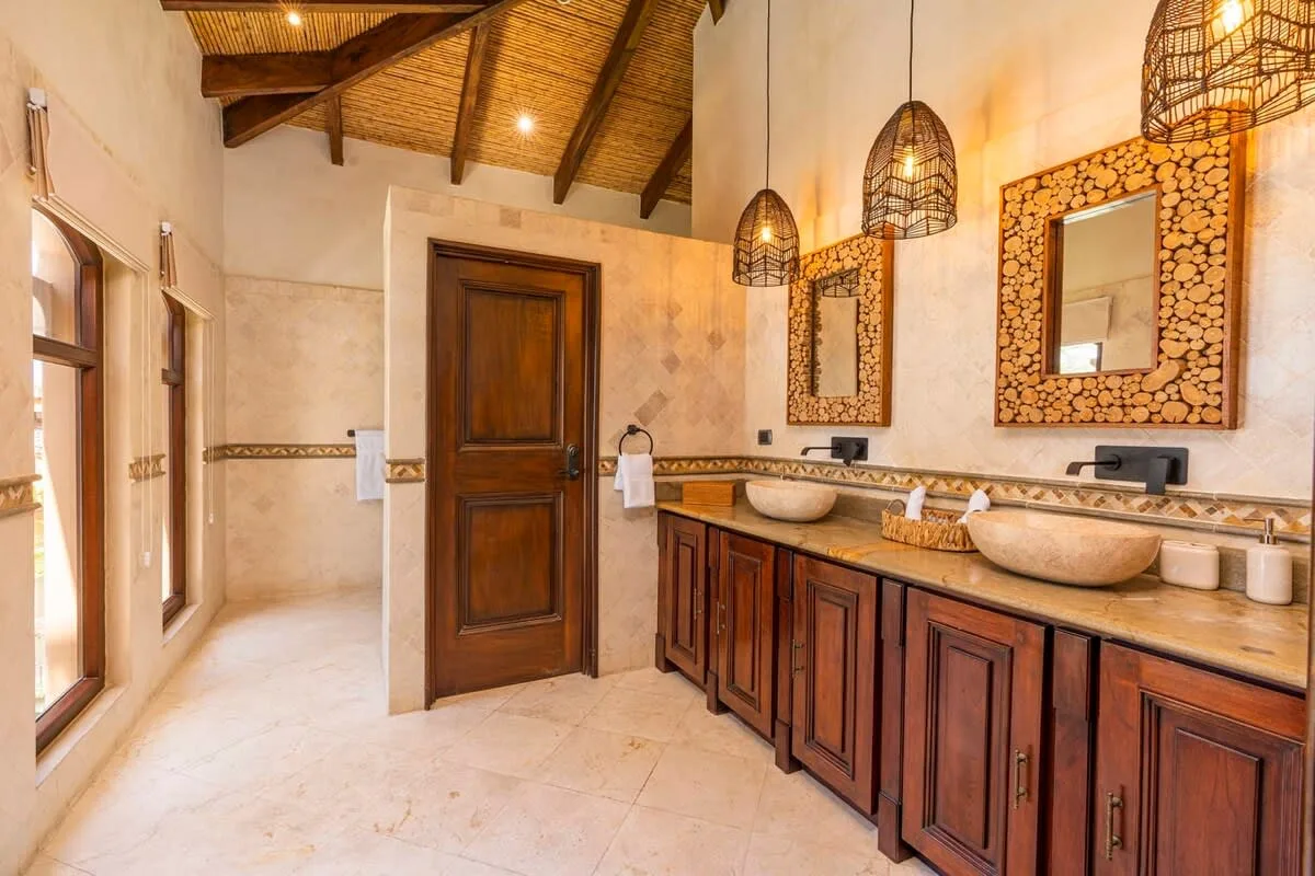 A bathroom with a long wooden vanity, vessel sinks, and woven pendant lights.