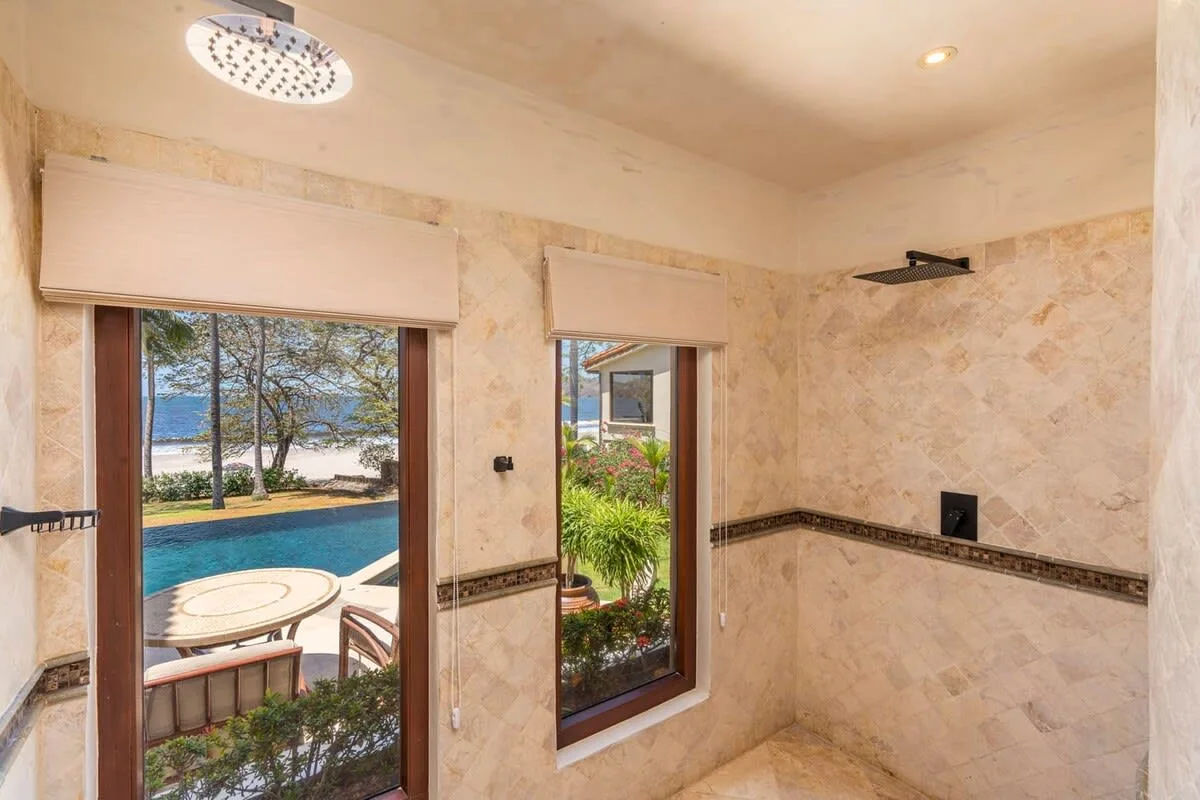 A tiled shower area with windows overlooking a pool and garden.