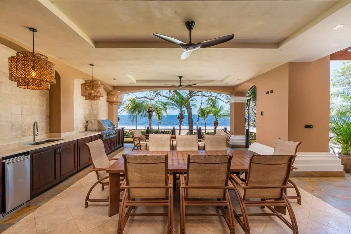 A covered dining area opens onto a patio with palm trees and ocean views.