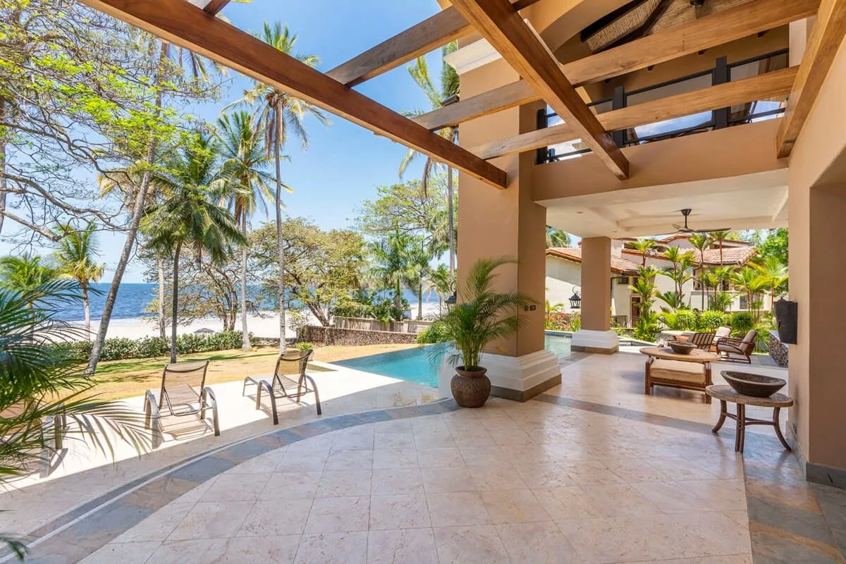 An open-air patio overlooks a pool, palm trees, and the ocean.