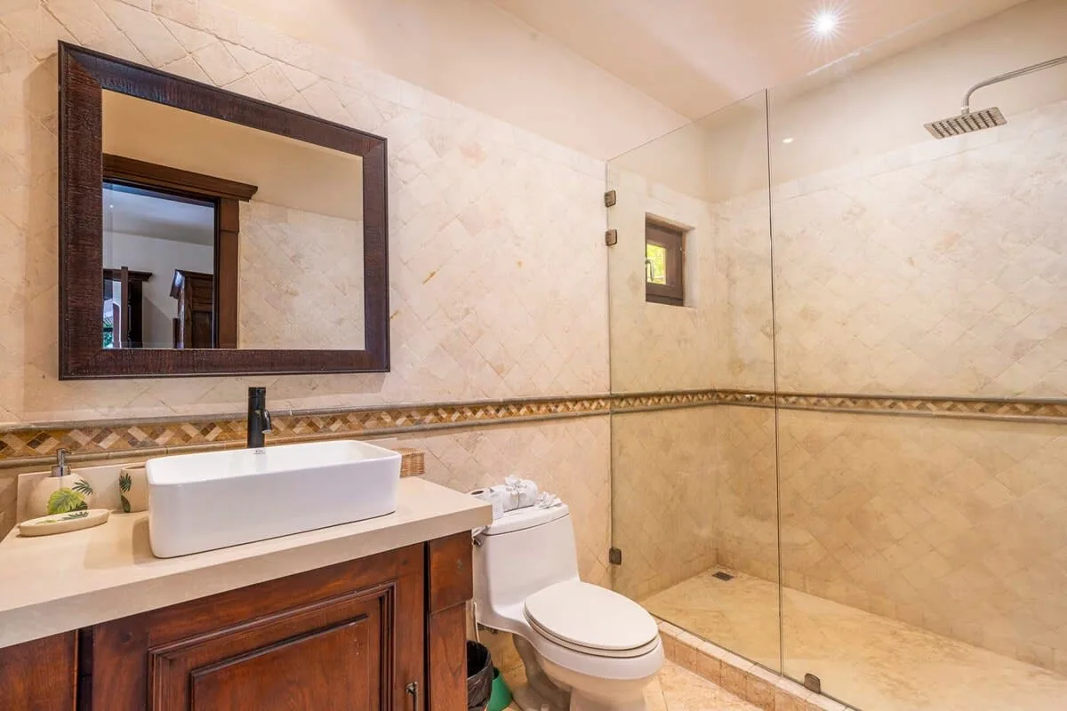 A tiled bathroom with a vanity, toilet, and glass shower.