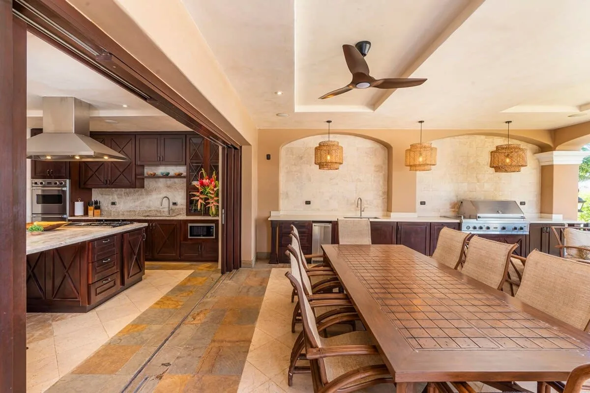 An open kitchen and dining area features a long wooden table and pendant lights.