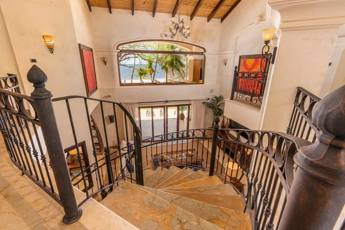 A curved staircase with dark railings overlooks a bright interior with a large window.