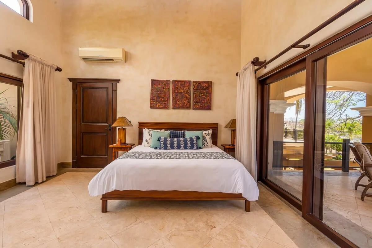 A bedroom with a bed centered between curtained windows and a glass door.