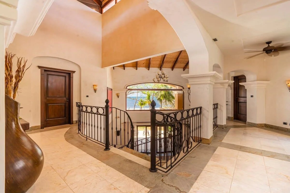 An interior landing has a black railing around a stairwell and an arched opening.