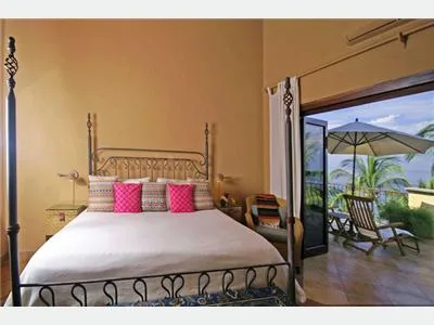 A bedroom with a metal-framed bed and pink cushions opens onto a furnished terrace.