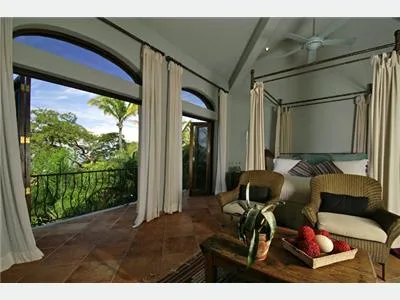 A sitting area with arched glass doors, cream curtains, two armchairs, and a low wooden table.