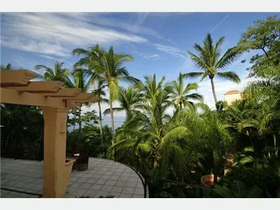 A tiled terrace overlooks dense tropical greenery and palm trees beneath a partly cloudy sky.