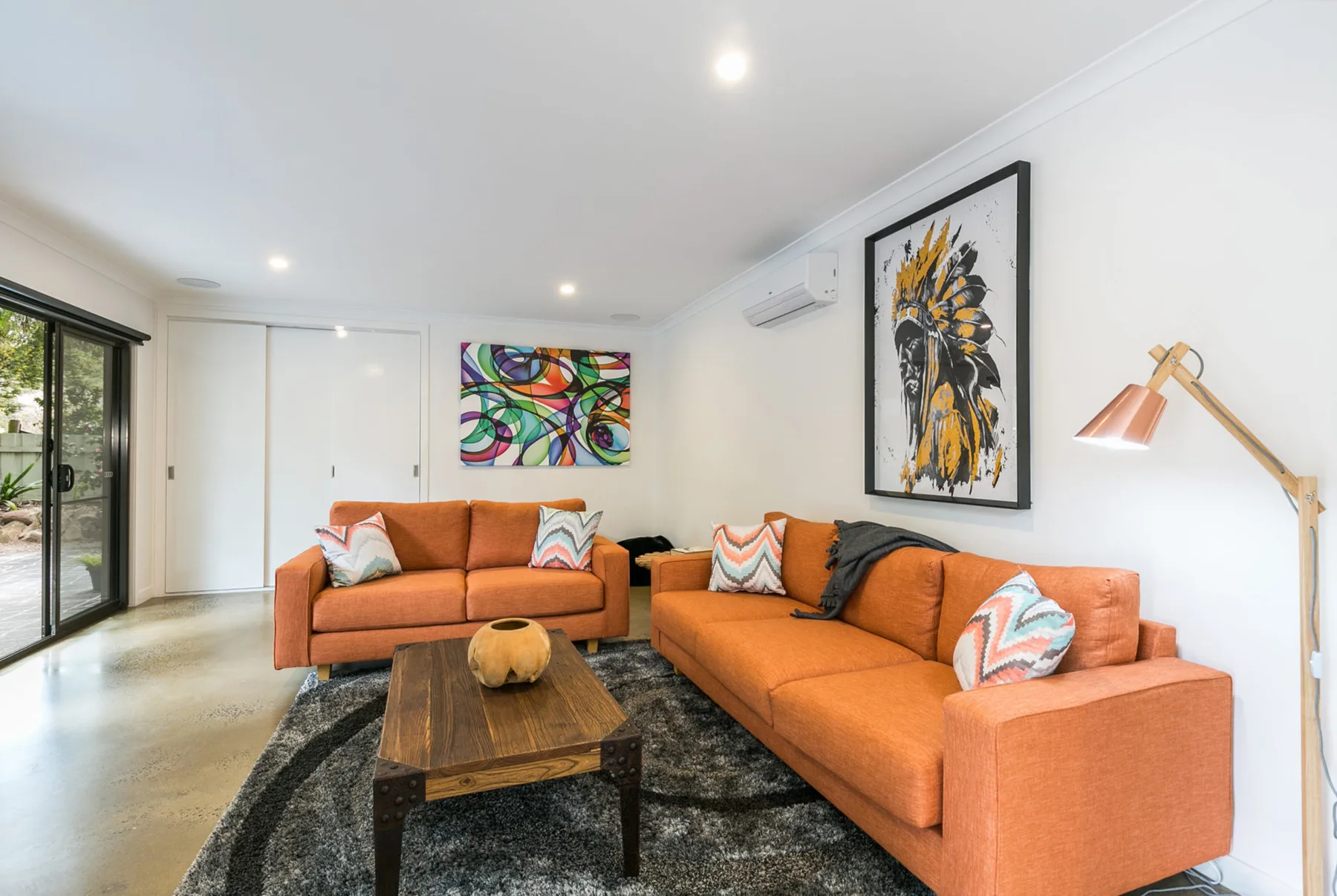 Una sala luminosa con asientos naranjas, obras de arte coloridas y una mesa de centro de madera.