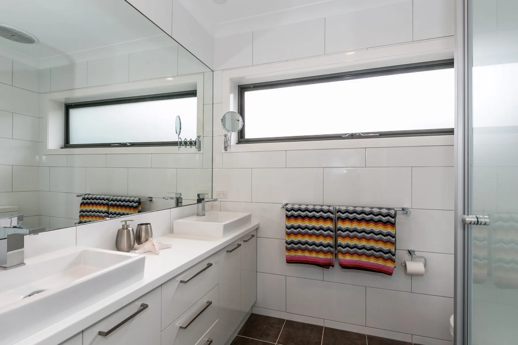 Un baño luminoso con azulejos, un tocador largo, espejo y ventanas translúcidas.