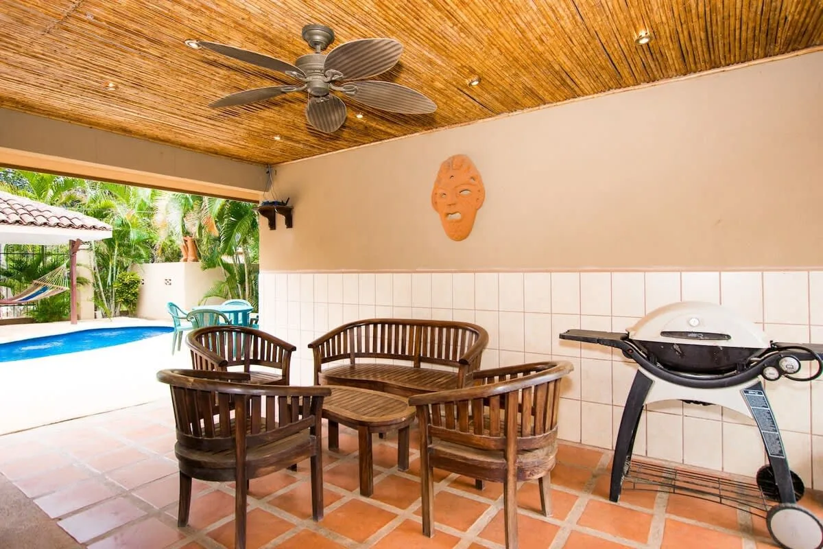 Shared amenity: A covered patio with wooden seating and a grill overlooks a swimming pool.