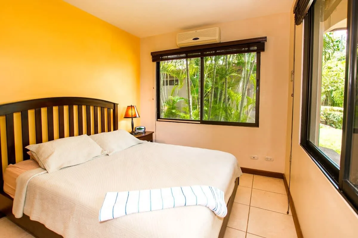 A bedroom with a bed beside a window overlooking greenery.