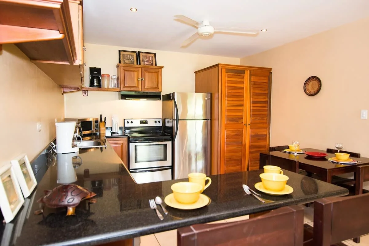 A kitchen with a central counter, stove, refrigerator, and wooden cabinets.