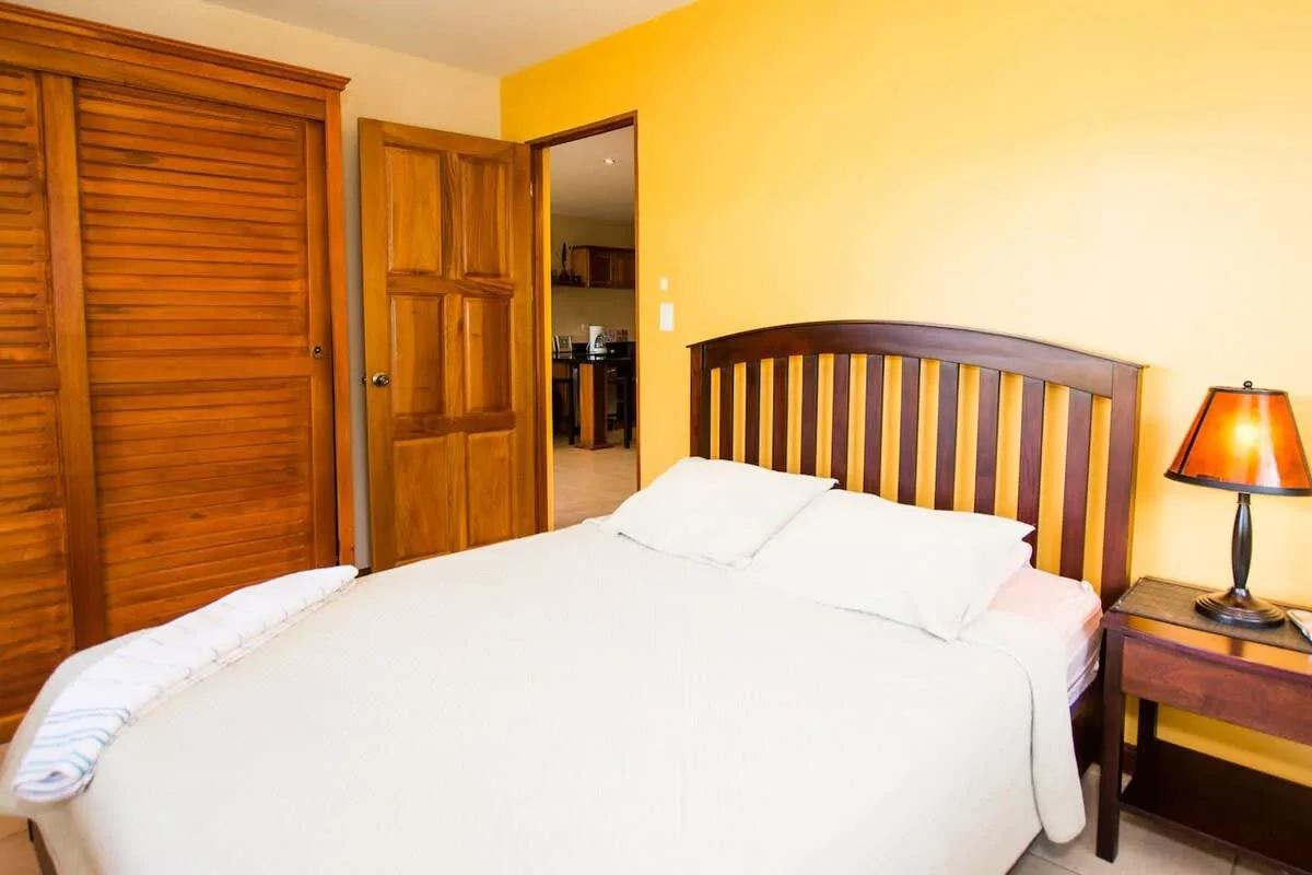 A bedroom with a neatly made bed, wooden headboard, and bedside lamp.