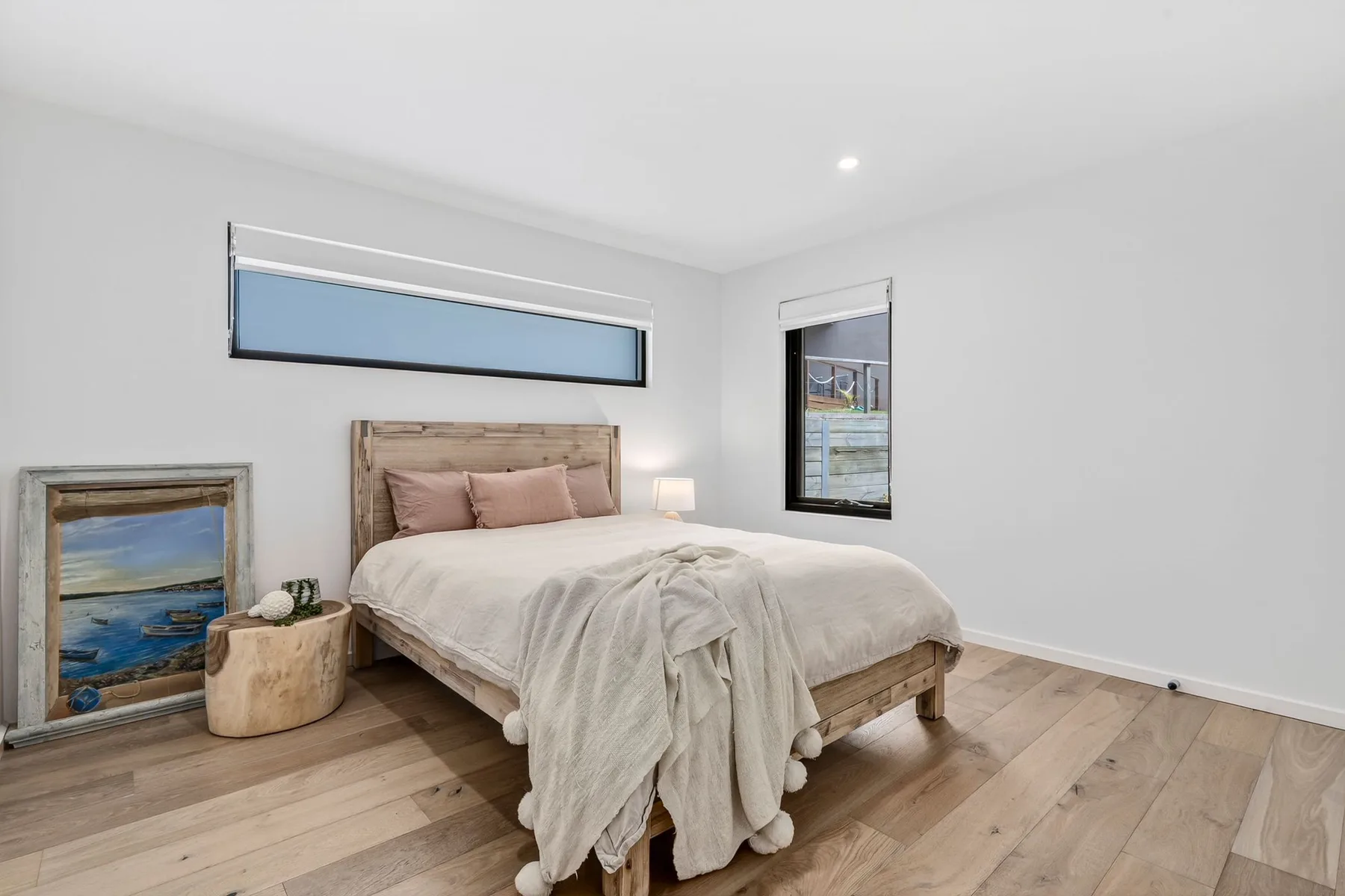 Un dormitorio luminoso con cama de madera, ropa de cama clara y ventanas estrechas.