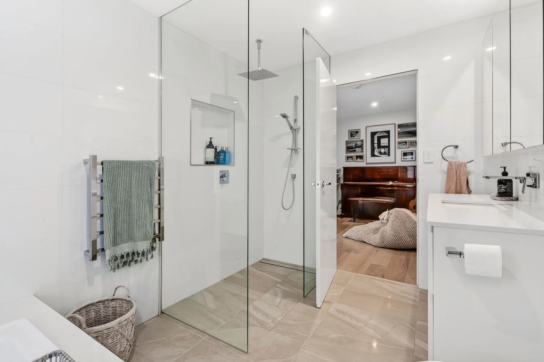 Un baño luminoso con ducha de cristal y un lavabo junto a la puerta abierta.