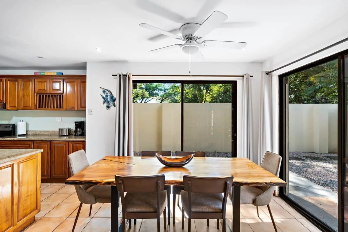Comedor con una mesa de madera junto a grandes ventanas y una cocina.