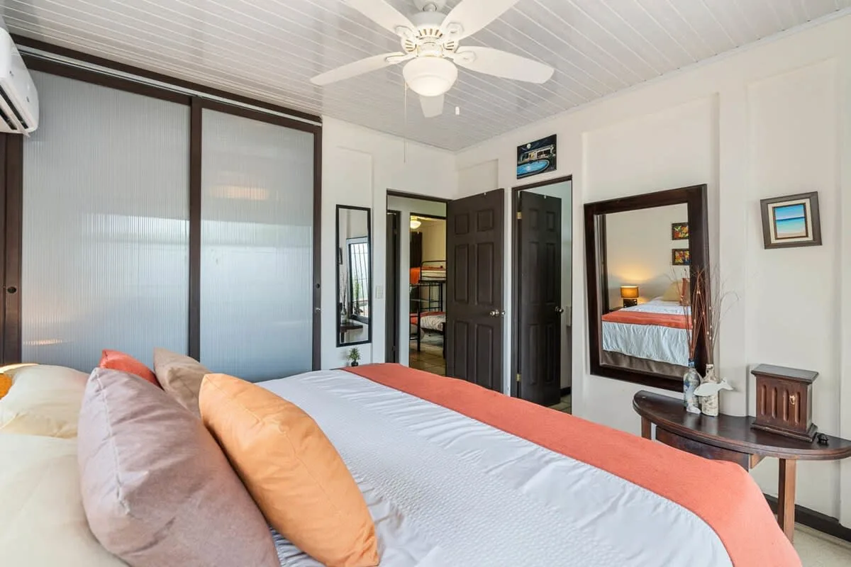 Un dormitorio con una cama, un ventilador de techo y puertas oscuras.