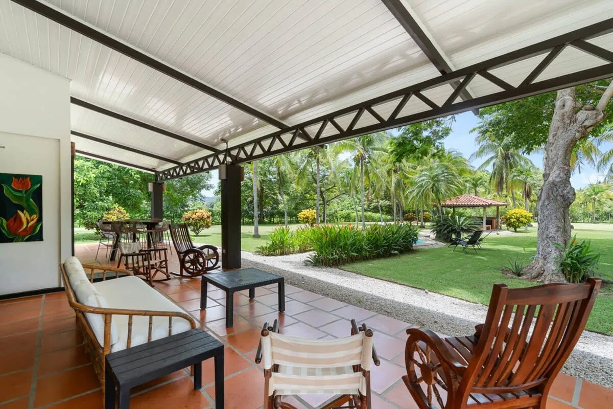 Un patio cubierto con asientos da a un jardín verde con palmeras.