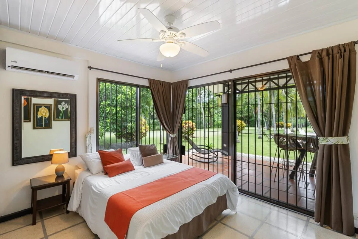Un dormitorio con una cama junto a grandes ventanas con vistas a un jardín.